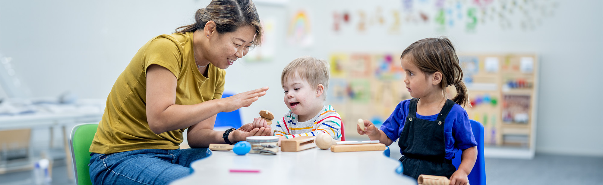 Zwei Kinder im Vorschulalter sitzen mit einer Pädagogin an einem Tisch.