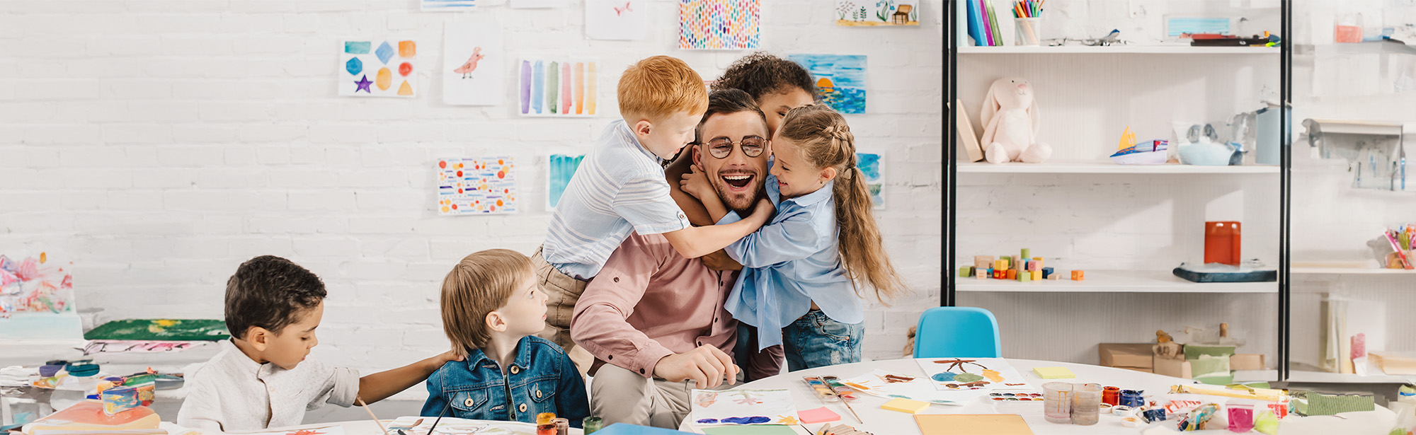 Männlicher Pädagoge mit einer Gruppe von Kindern im Kindergarten beim Malunterricht