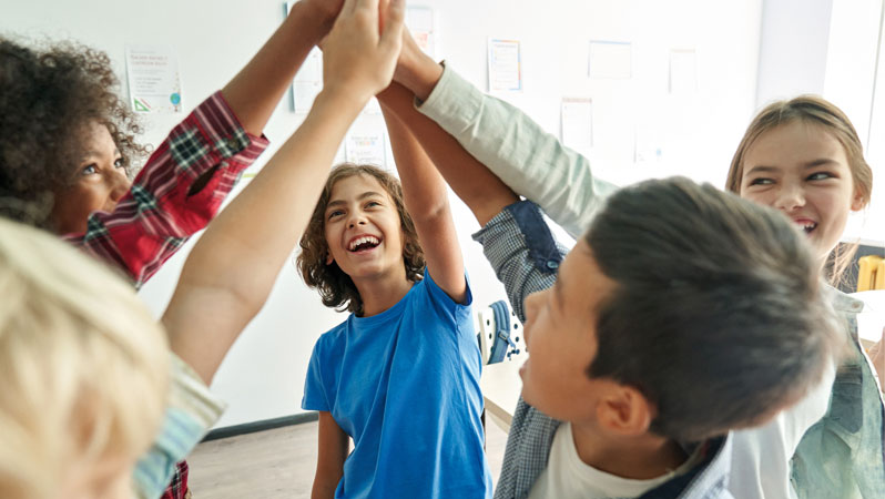 Die Hände mehrerer Schülerinnen und Schüler berühren sich bei ausgestrecktem Arm zum motivierenden Gruß